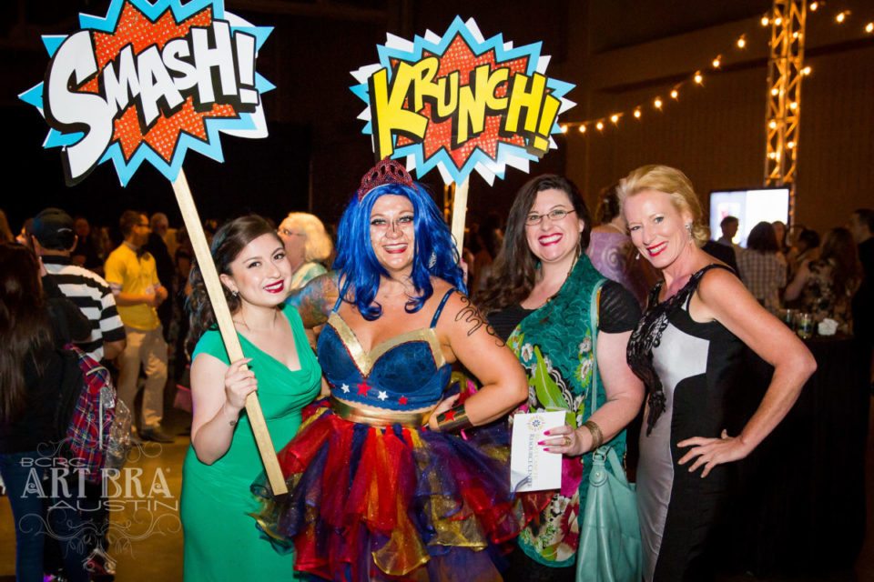 4 women posing in costumes and holding comic book signs